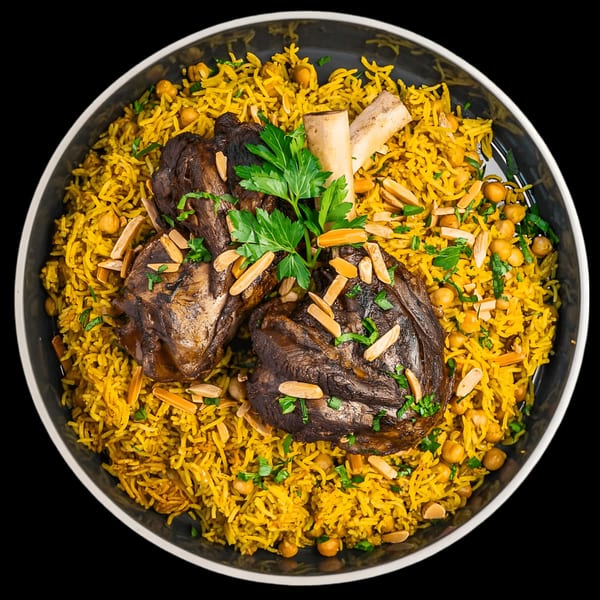 Overhead view of a Mediterranean lamb shank dish with yellow rice, chickpeas, almonds, and parsley.