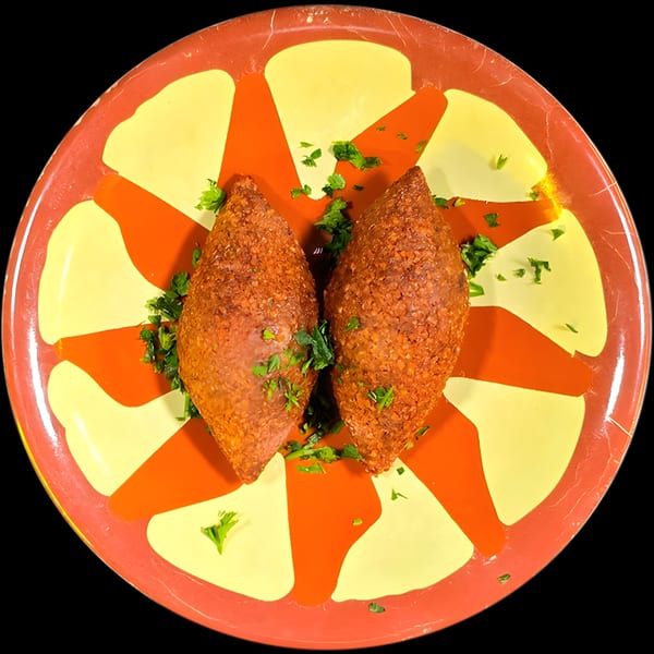 Two golden-brown kibbeh, garnished with fresh parsley, on a vibrant red and yellow patterned plate.