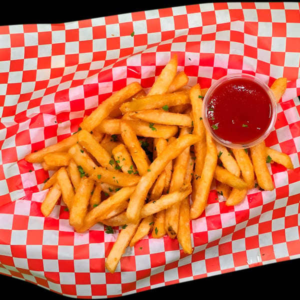 Golden french fries with parsley flakes and a side of ketchup in a red and white checkered basket.