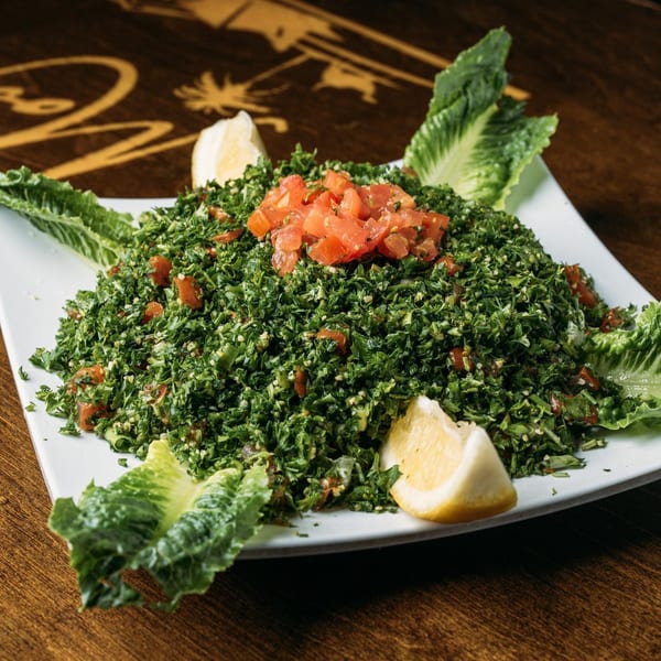 A fresh tabbouleh salad with chopped parsley, tomatoes, and lemon wedges on a white plate.